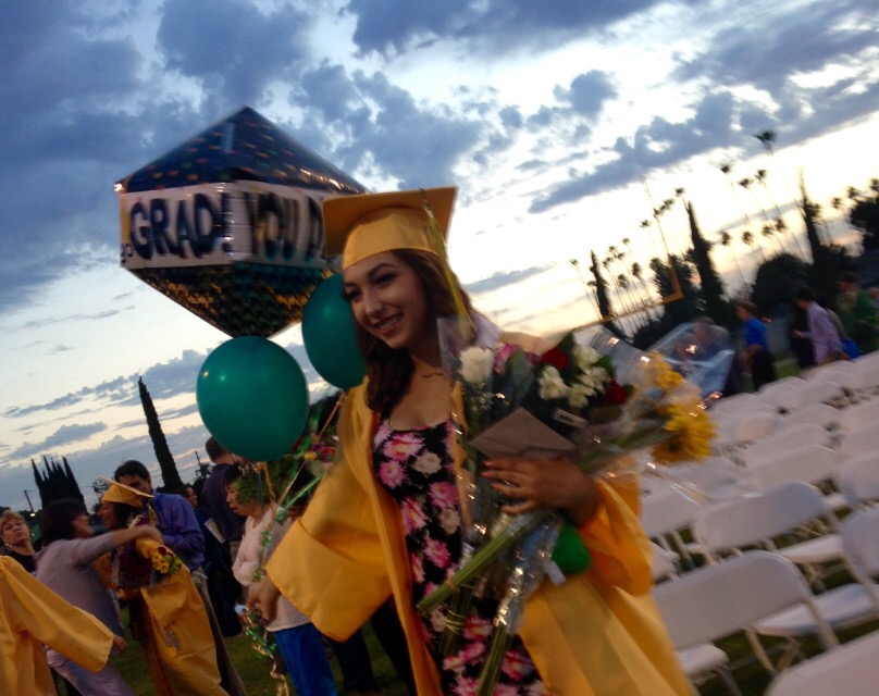 young lady in graduation cap and gown, holding balloons